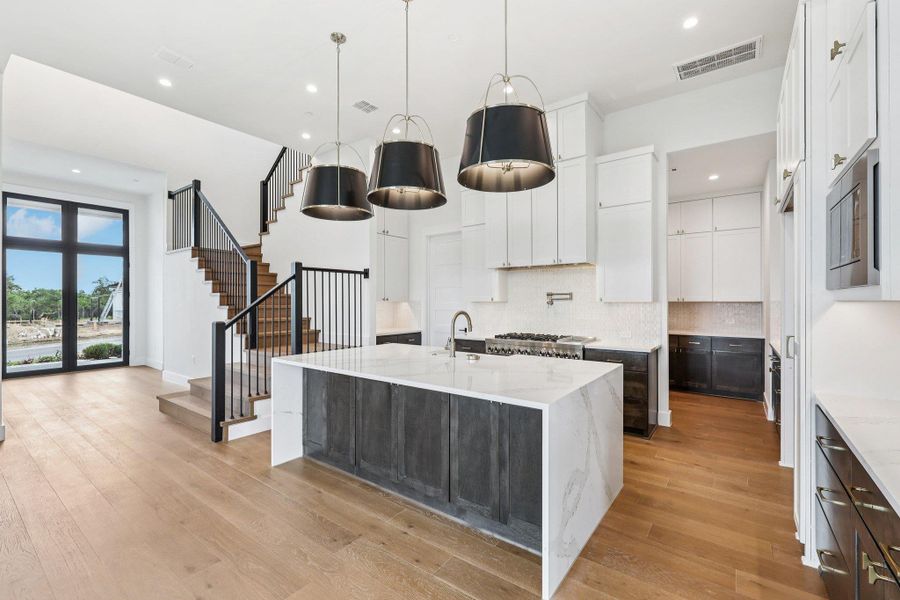 Kitchen featuring decorative backsplash, light stone countertops, light wood finished floors, a center island with sink, and white cabinetry