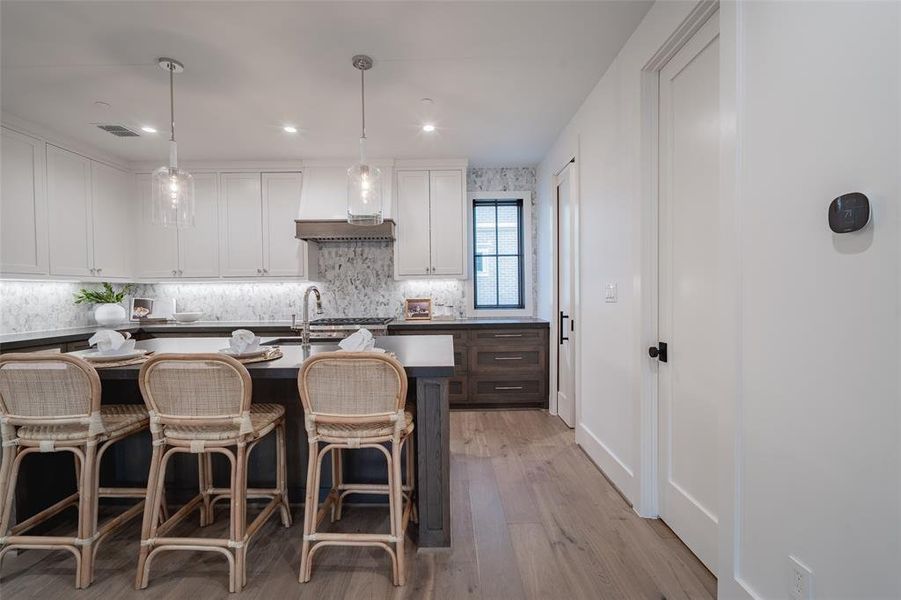 Kitchen featuring decorative light fixtures, an island with sink, white cabinets, custom exhaust hood, and light hardwood / wood-style floors