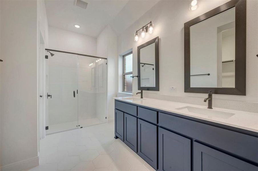 Spacious bathroom featuring a dual vanity with white countertops and dark cabinetry, individual framed mirrors, and a glass-enclosed shower with dark hardware