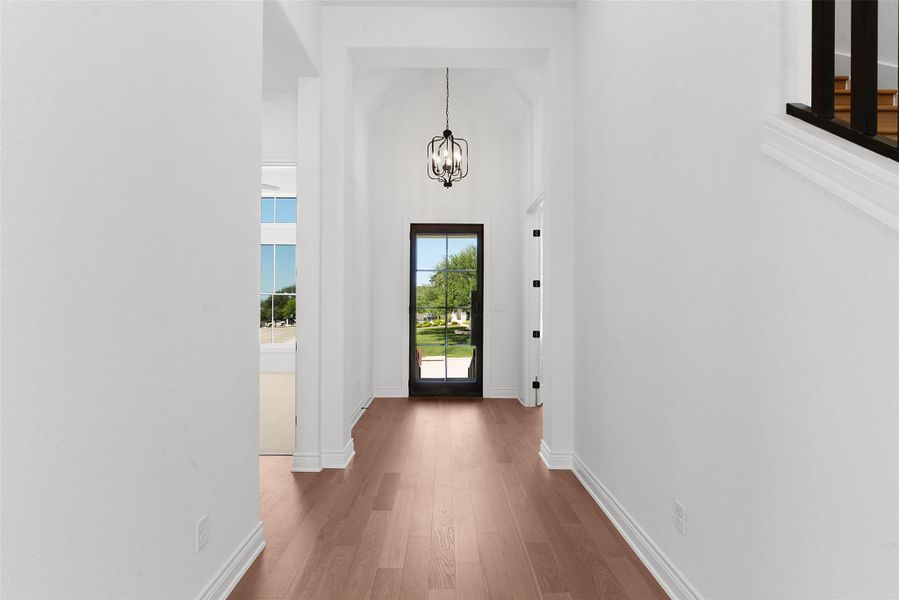 A welcoming entryway with rich wood flooring leads to a brightly lit front door and graceful chandelier.