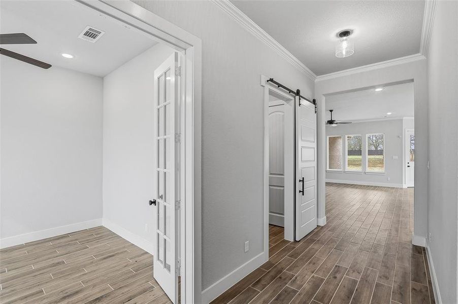 Corridor featuring a barn door, wood tiled floors, crown molding, and recessed lighting