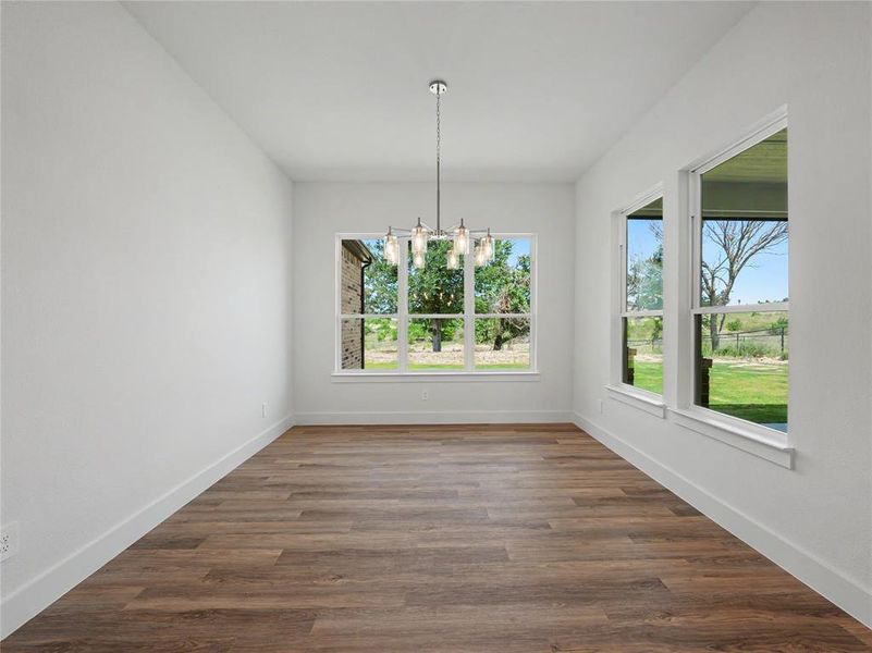 Spacious room featuring wood-finish flooring, white baseboards, and a contemporary chandelier