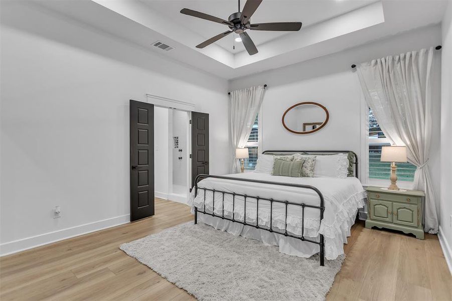 Primary Bedroom featuring a raised ceiling, wood shutters and light wood-style flooring. Primary Bedroom featuring a raised ceiling, wood shutters and light wood-style flooring.