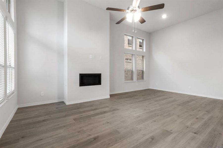 Unfurnished living room featuring wood finished floors, a fireplace, ceiling fan, and a towering ceiling Unfurnished living room featuring wood finished floors, a fireplace, ceiling fan, and a towering ceiling