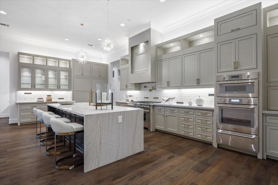 Exceptional chef’s kitchen showcasing top-of-the-line appliances, an oversized waterfall-edge island with integrated sink, and extensive custom cabinetry—designed for both beauty and function with generous storage throughout.