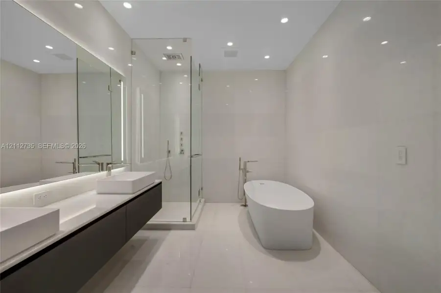 Floating dual vanity featuring rectangular vessel sinks, floor-to-ceiling stone-tiled walls, glass-enclosed shower, and a freestanding soaking tub