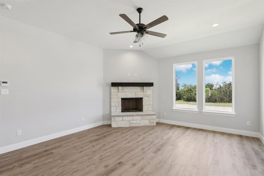 Unfurnished living room featuring wood-type flooring, a stone fireplace, vaulted ceiling, and ceiling fan