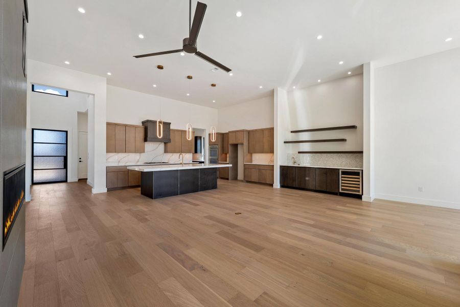 Kitchen featuring a high ceiling, open floor plan, hanging light fixtures, a kitchen island with sink, and tasteful backsplash