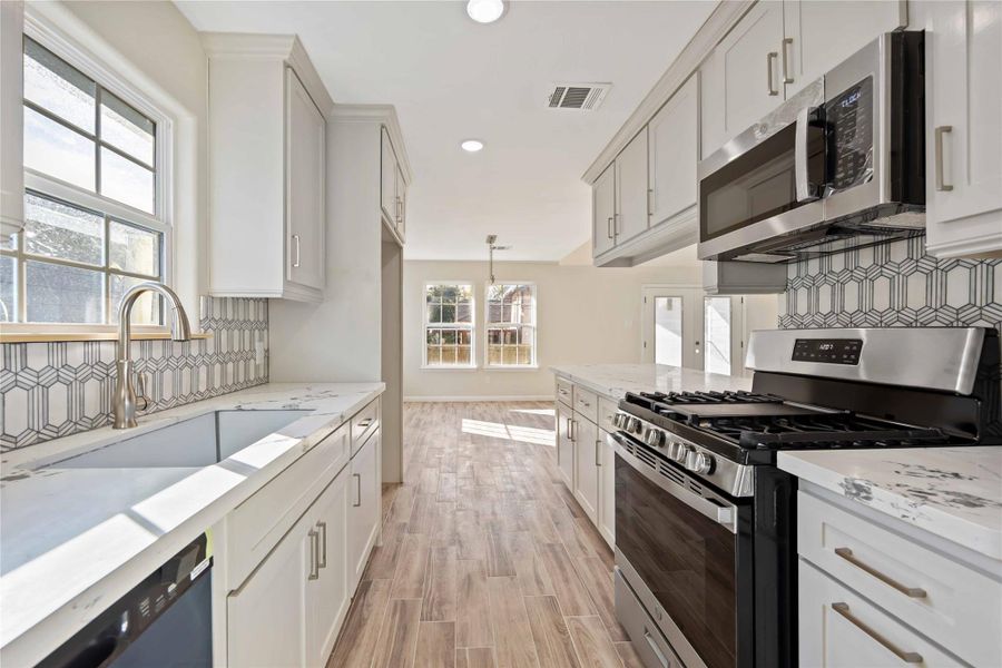 Modern kitchen with marble countertops, stainless steel stove, microwave, and dishwasher.