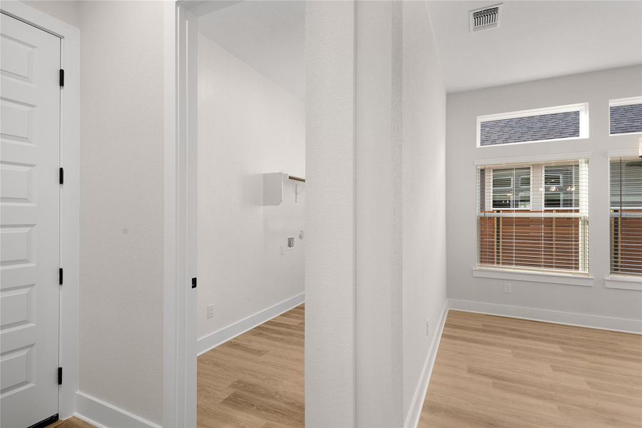 A well-lit laundry area with wood-look flooring connects seamlessly to a bright living space. A well-lit laundry area with wood-look flooring connects seamlessly to a bright living space.