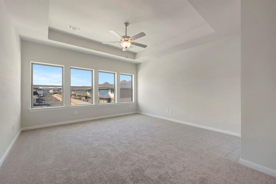 Unfurnished room with ceiling fan, light colored carpet, and a tray ceiling