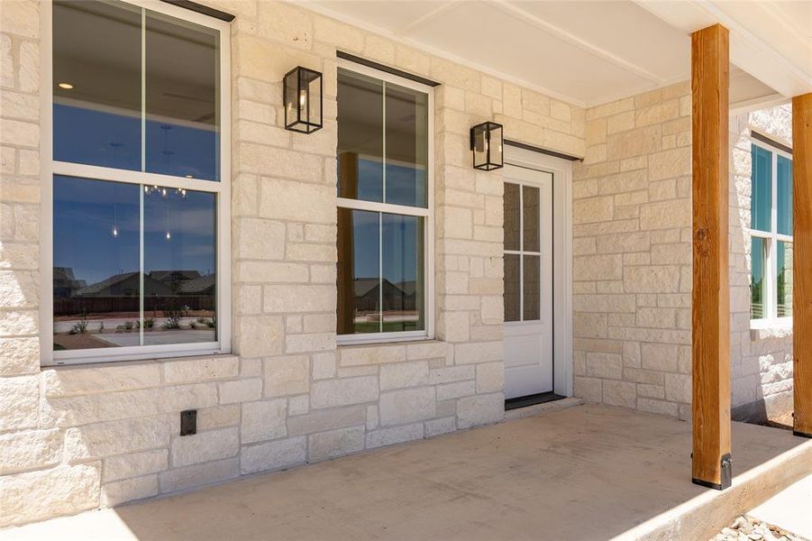 Stone veneer exterior featuring a covered patio, natural wood columns, white grid windows, and a white paneled door with glass inserts