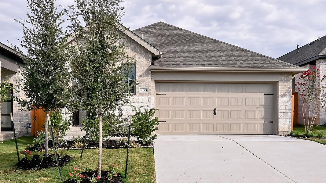 View of front of home with a shingled roof, stone siding, driveway, and a garage