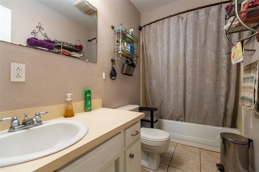 Bathroom featuring shower / bath combo with shower curtain, light tile patterned floors, vanity, and a textured wall Bathroom featuring shower / bath combo with shower curtain, light tile patterned floors, vanity, and a textured wall