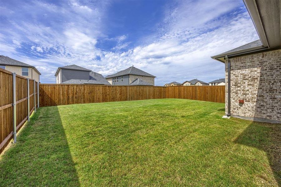 Expansive grassy backyard featuring a full privacy fence, brick exterior siding, and a partial covered patio area