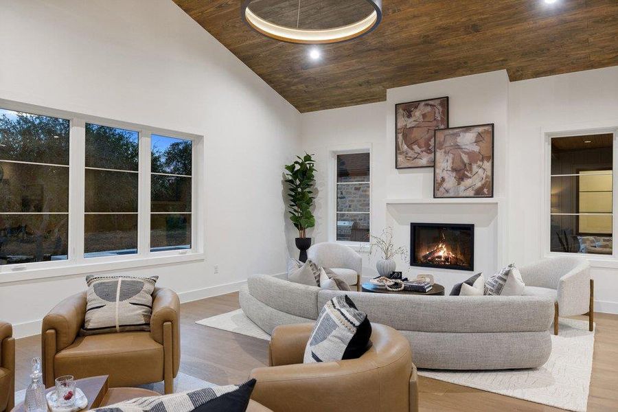 A refined living space showcasing a cozy fireplace, light wood flooring, and a unique wood-paneled vaulted ceiling.