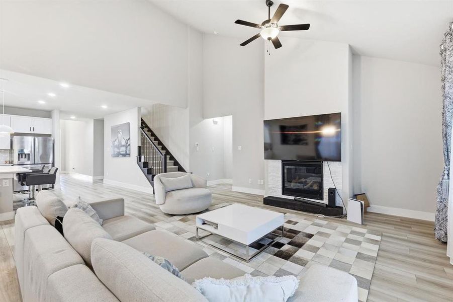 Living room with high vaulted ceiling, light wood-style flooring, stairway, a glass covered fireplace, and a ceiling fan