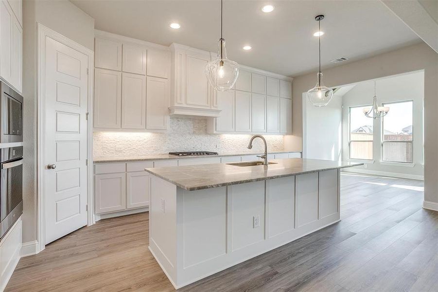 Kitchen featuring white cabinetry, sink, hanging light fixtures, stainless steel appliances, and a kitchen island with sink