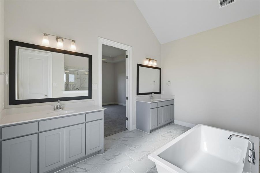 Bathroom featuring light marble finish floors, two vanities, a freestanding tub, a marble finish shower, and high vaulted ceiling Bathroom featuring light marble finish floors, two vanities, a freestanding tub, a marble finish shower, and high vaulted ceiling