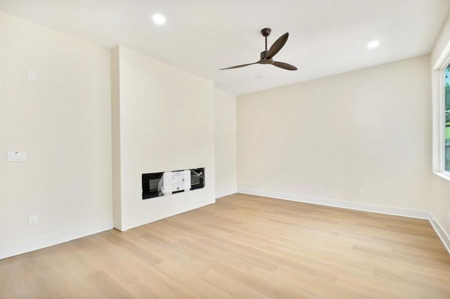 Unfurnished living room featuring ceiling fan, a fireplace, and light wood-type flooring