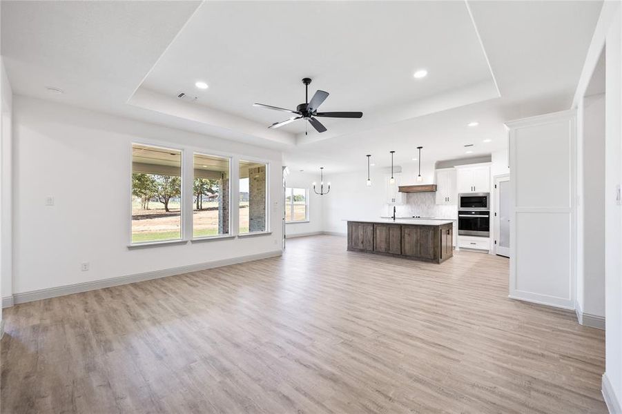 Unfurnished living room featuring a tray ceiling, a chandelier, light wood finished floors, and recessed lighting