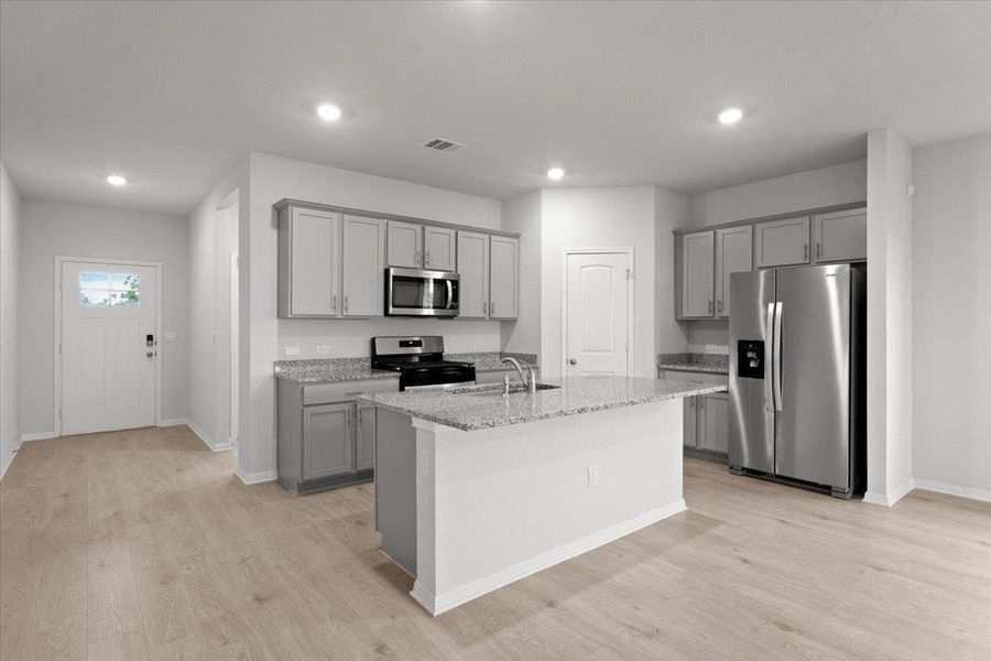 Open concept kitchen featuring an island with a stainless steel sink, granite countertops, light gray cabinetry, and wood-finish flooring