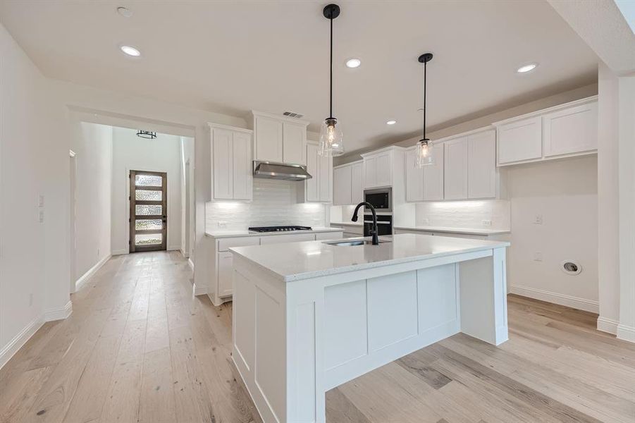 Kitchen featuring pendant lighting, sink, a center island with sink, white cabinetry, and light wood-type flooring