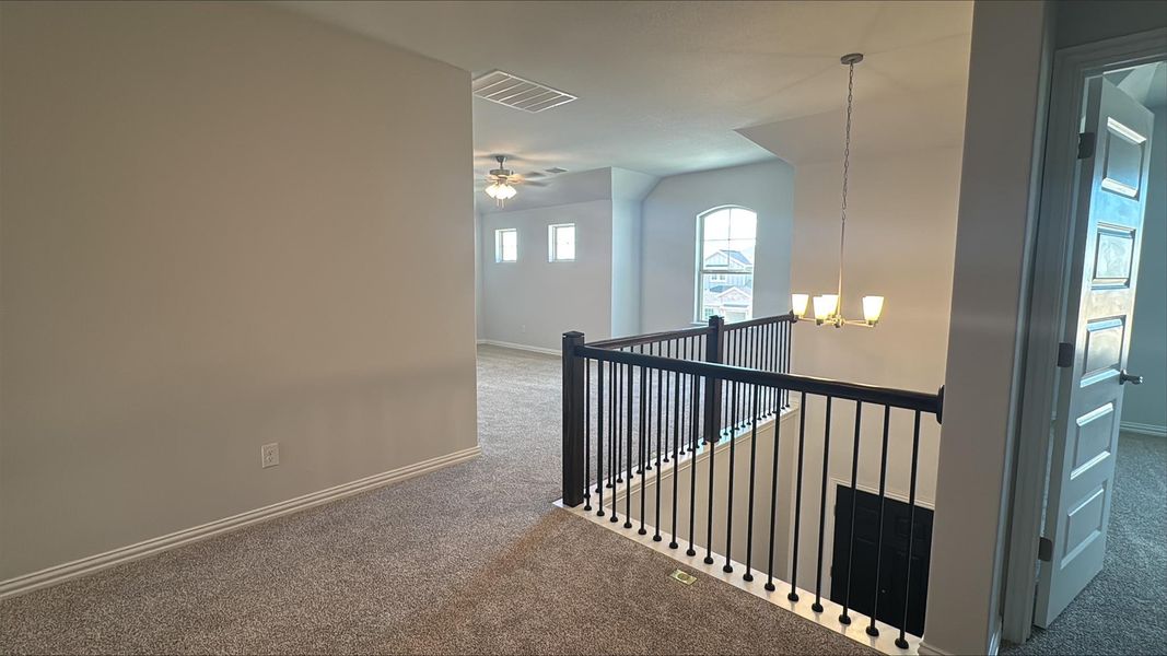Hallway featuring a chandelier, an upstairs landing, and carpet floors Hallway featuring a chandelier, an upstairs landing, and carpet floors