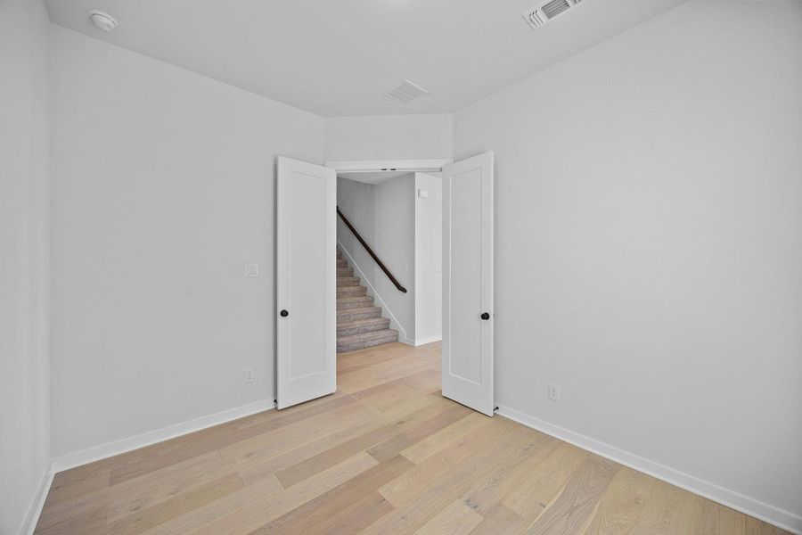 Spare room with light wood-style floors, stairway, and a smoke detector Spare room with light wood-style floors, stairway, and a smoke detector