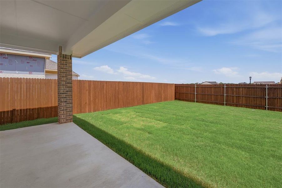 Expansive backyard featuring a covered concrete patio, lush green lawn, and a privacy fence Expansive backyard featuring a covered concrete patio, lush green lawn, and a privacy fence