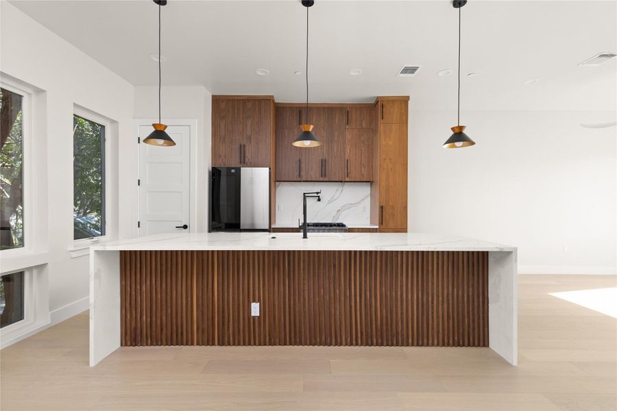 A spacious waterfall island anchors this modern kitchen featuring warm wood cabinetry and light hardwood flooring.