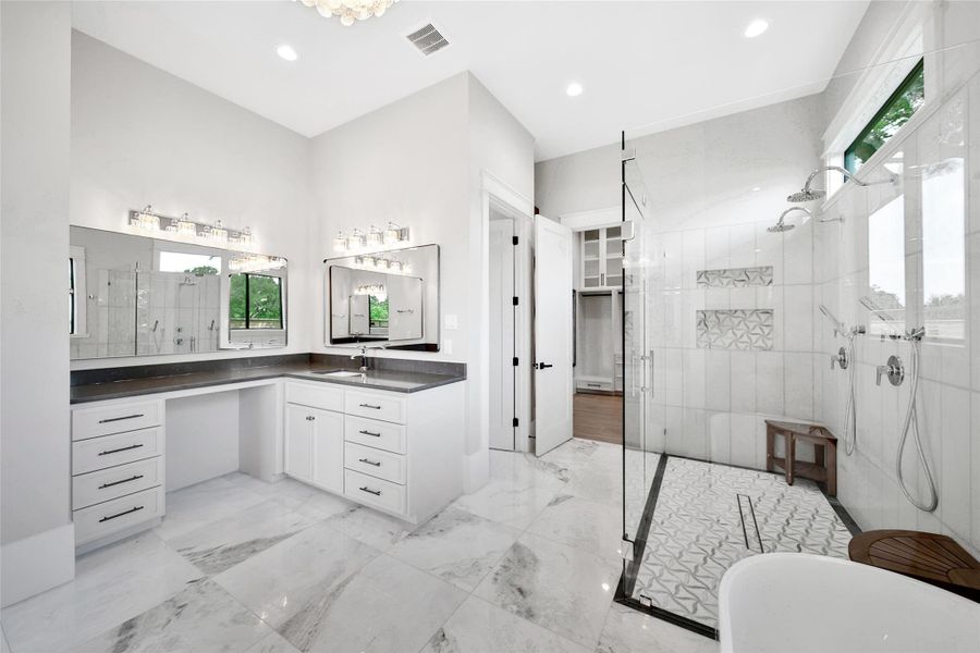 Beautiful stone countertops is paired with natural stone flooring, while the frameless glass shower helps to showcase custom tile work and finishes.