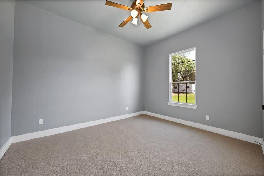 Carpeted room with a ceiling fan and a window overlooking exterior greenery