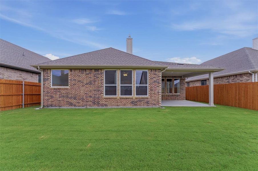 Expansive backyard featuring a manicured lawn, brick exterior, covered patio, and wood privacy fencing