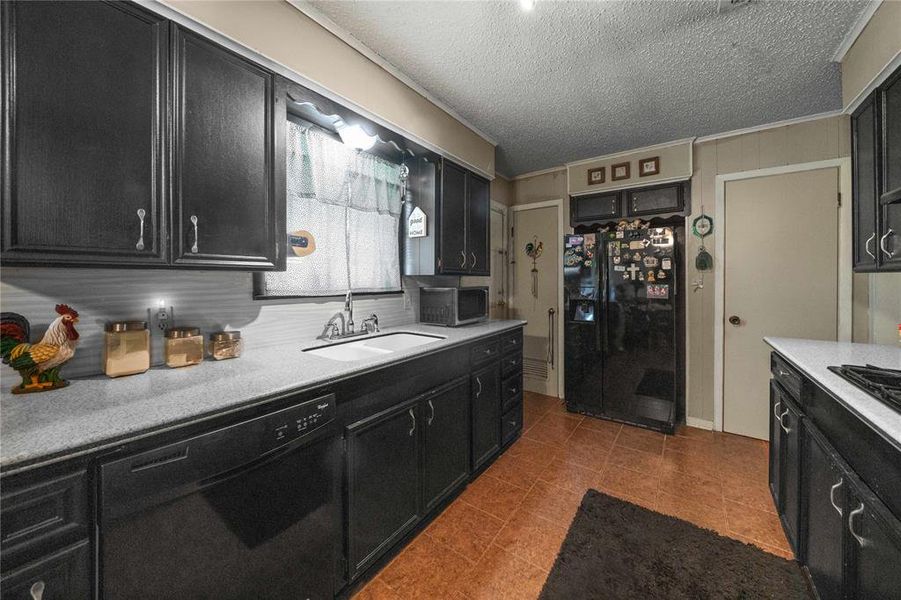 Kitchen with black appliances, dark cabinets, light countertops, dark tile patterned floors, and a textured ceiling