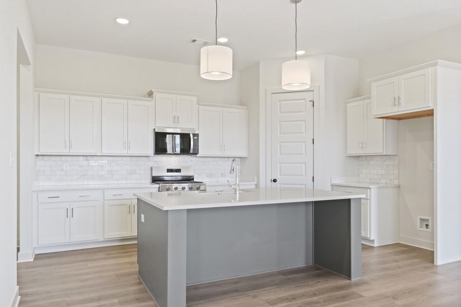 Two tone kitchen featuring two tone color scheme, stainless steel appliances, a center island with sink, backsplash, and light wood-style floors