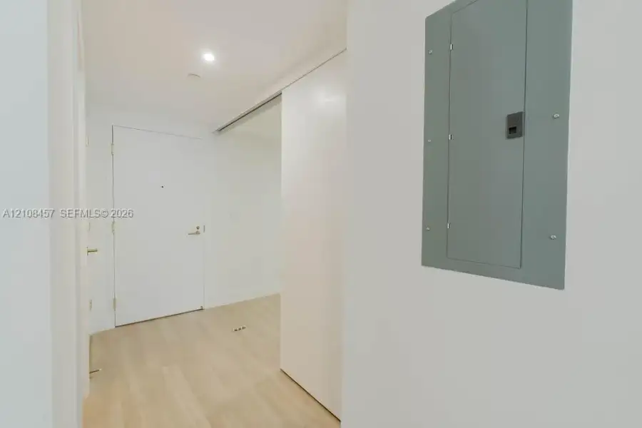 Interior entrance featuring light-toned wood-finish flooring, a solid core entry door with metallic hardware, recessed ceiling lighting, and a white sliding door Interior entrance featuring light-toned wood-finish flooring, a solid core entry door with metallic hardware, recessed ceiling lighting, and a white sliding door