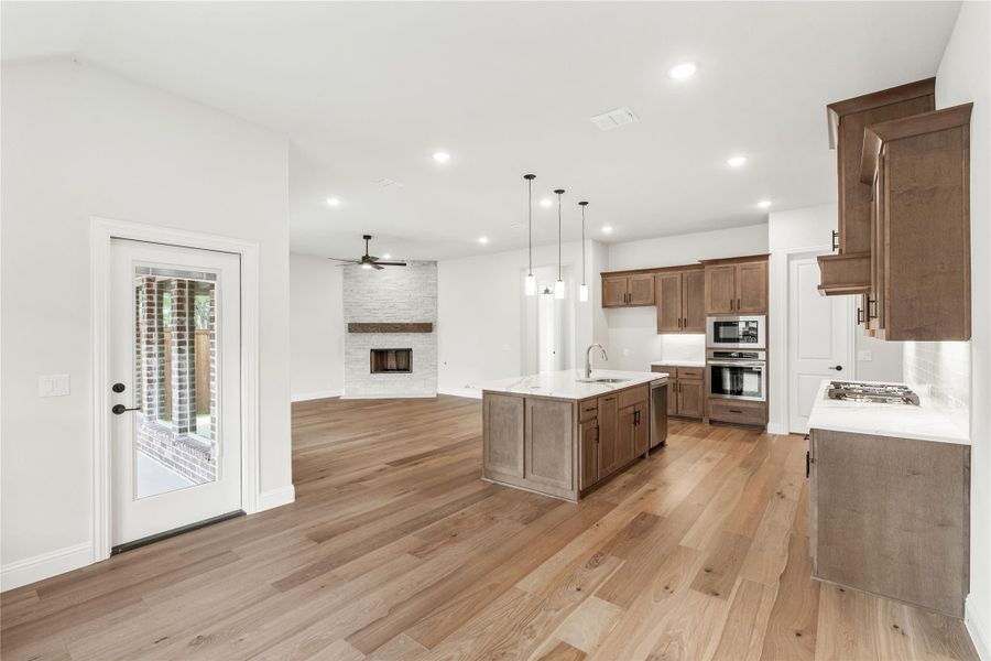 Open-concept kitchen and living area with wood cabinets, center island, hardwood floors, and stone fireplace