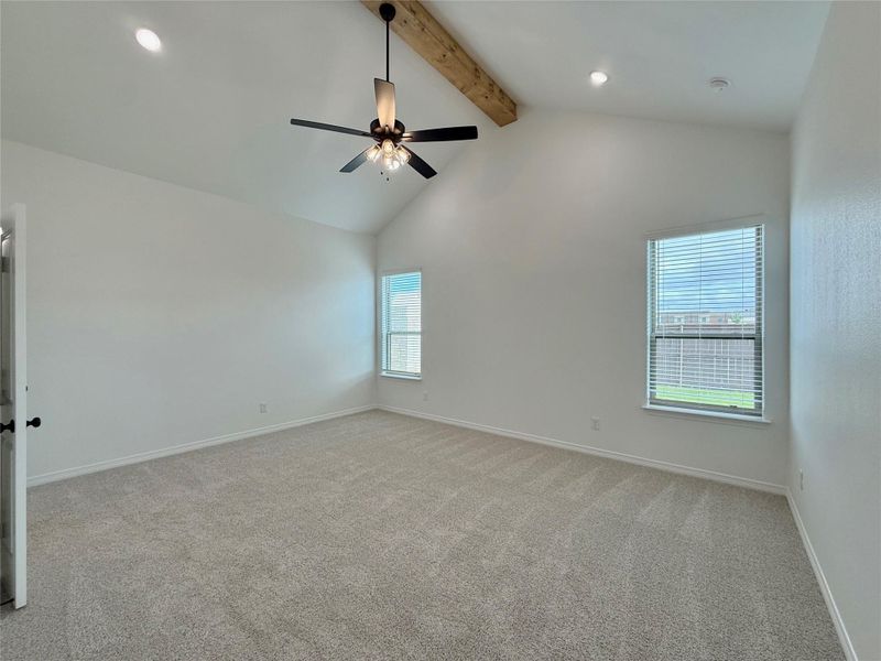 Spacious room featuring a vaulted ceiling with a prominent wood beam accent and a ceiling fan