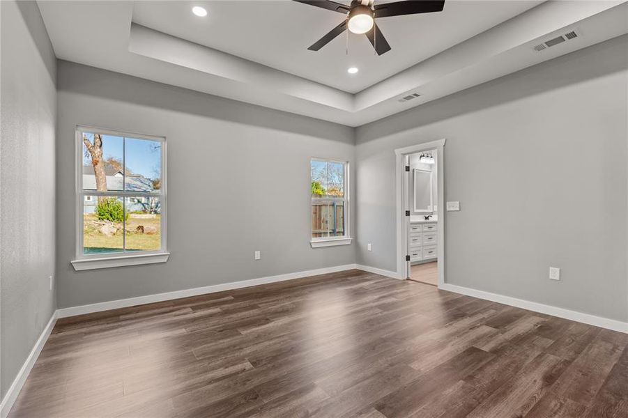 Unfurnished bedroom featuring dark wood-type flooring, a tray ceiling, ceiling fan, and recessed lighting
