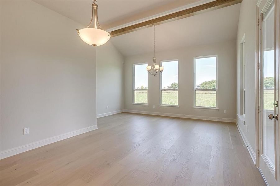 Unfurnished room with vaulted ceiling with beams, an inviting chandelier, and light hardwood / wood-style flooring