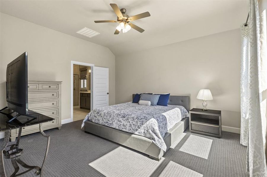 Carpeted bedroom with a ceiling fan, lofted ceiling, baseboards, and ensuite bathroom