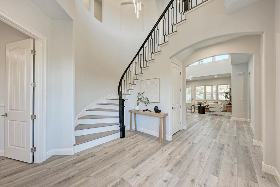 Foyer with arched walkways, stairs, a high ceiling, and light wood-style floors