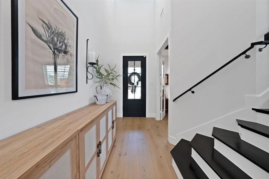 Entryway featuring a dark paneled front door, wood-finish flooring, and a contemporary staircase with dark treads and a black metal handrail Entryway featuring a dark paneled front door, wood-finish flooring, and a contemporary staircase with dark treads and a black metal handrail