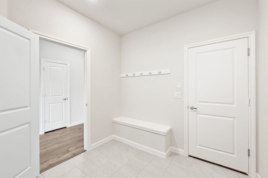 Mudroom with built-in bench, wall coat hooks, white doors, and light tile flooring