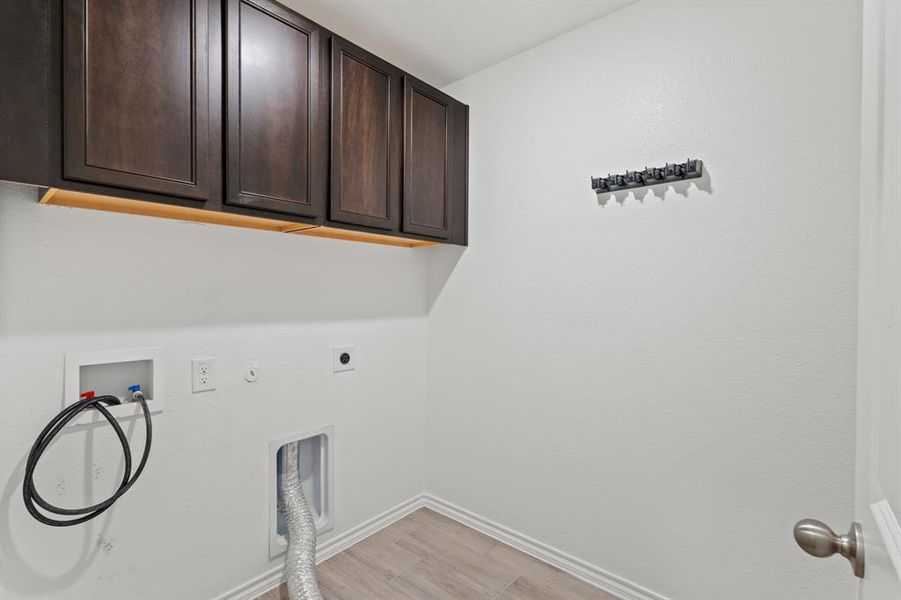 Laundry area featuring light wood-type flooring, gas dryer hookup, cabinet space, electric dryer hookup, and washer hookup Laundry area featuring light wood-type flooring, gas dryer hookup, cabinet space, electric dryer hookup, and washer hookup