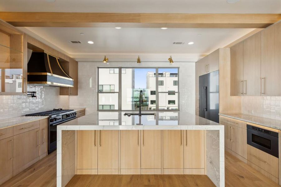 Kitchen with black gas stove, wall chimney exhaust hood, high end refrigerator, a sink, and light brown cabinetry