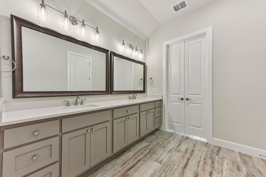 Bathroom featuring double vanity, light wood-style floors, and vaulted ceiling