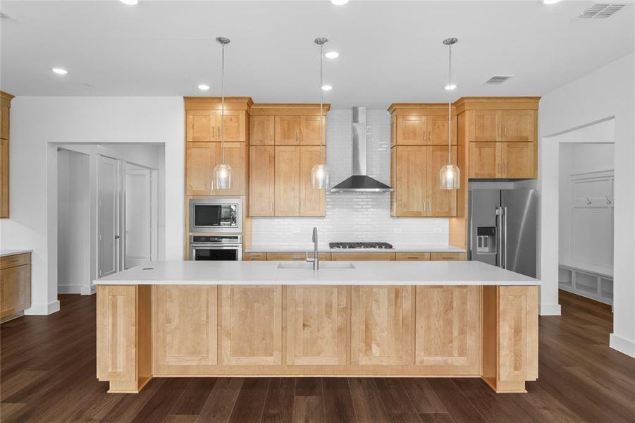 Kitchen featuring a large central island with a white countertop, light wood-finish cabinetry, stainless steel appliances, a tile backsplash, and dark wood-finish flooring