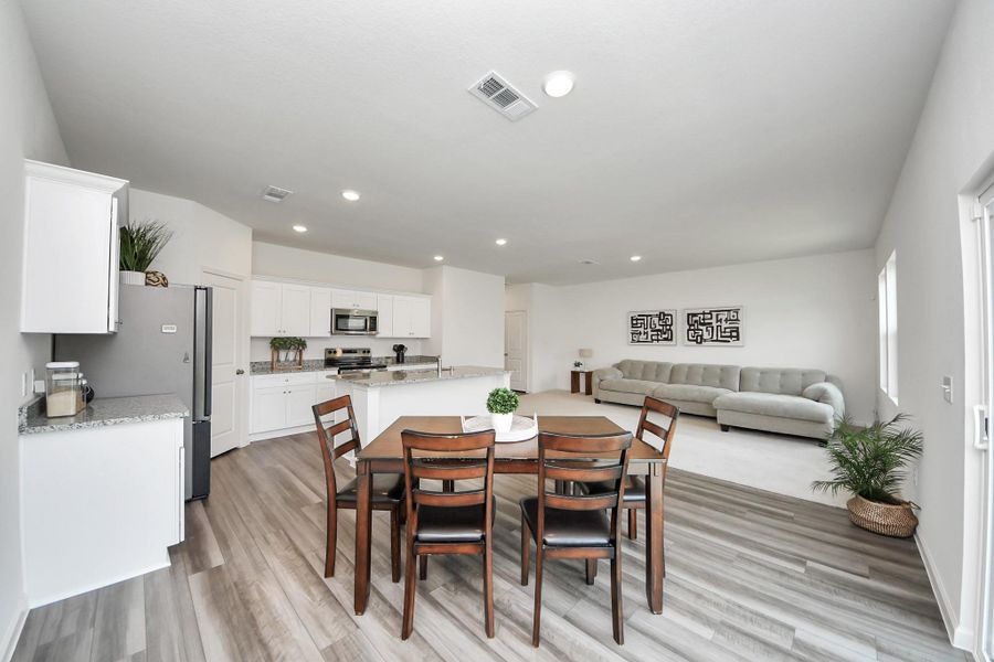 Spacious open-concept living area with a modern kitchen featuring white cabinetry and granite countertops, flowing seamlessly into a cozy living room and dining space with stylish wood flooring.
